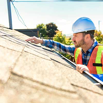 Worker with a white hard hat and orange vest inspecting a residential roof